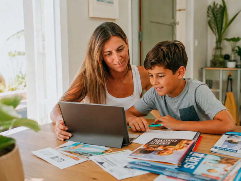 Madre revisando opciones de actividades extraescolares con su hijo sentados a la mesa en verano