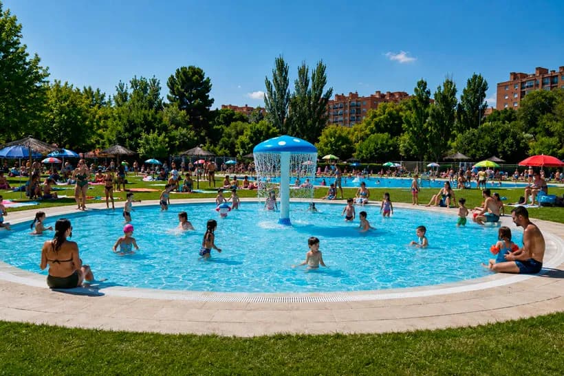 Vaso infantil de una piscina municipal de verano en Madrid con familias y sombrillas en el césped