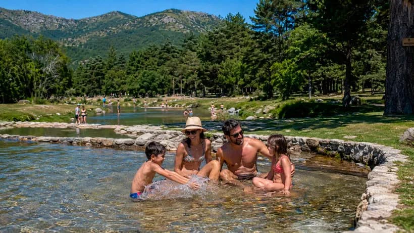 Familia con niños bañándose en una piscina natural de la sierra de Madrid rodeada de pinos